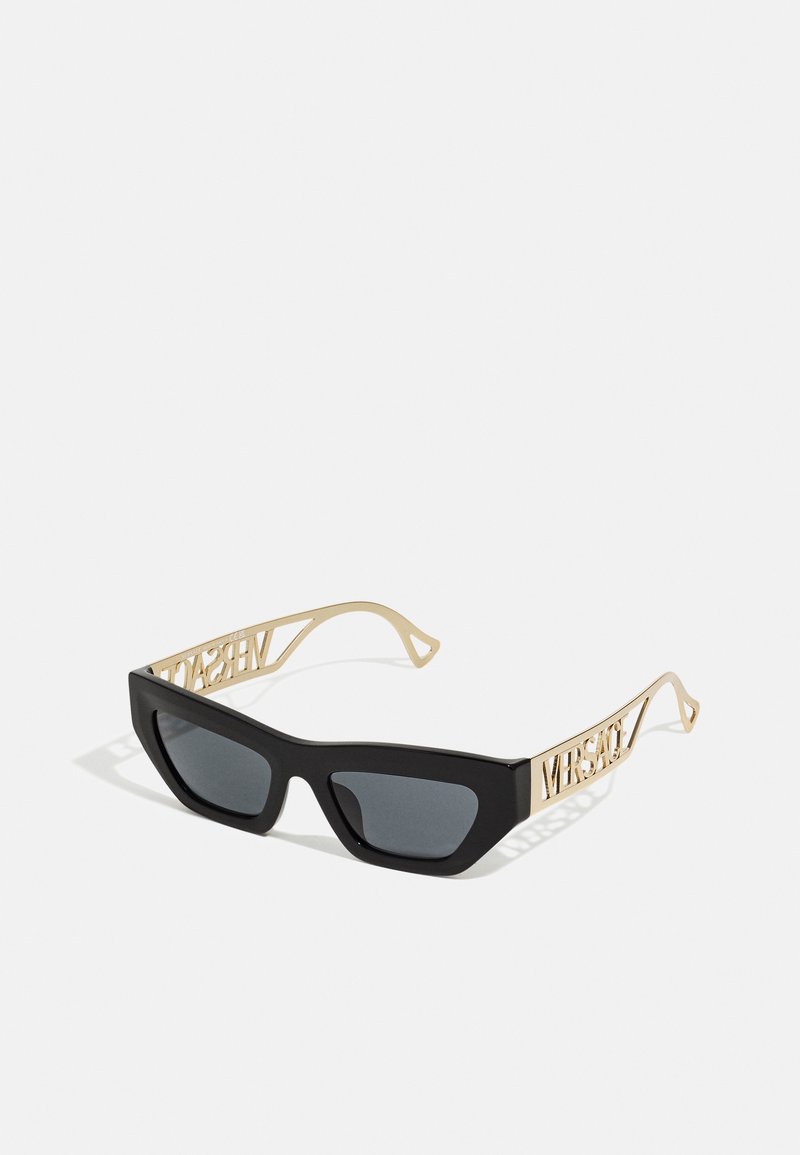 Schwarze Kunststoff-Sonnenbrille mit gewinkelten Fassung, grauen Gläsern und goldfarbenen, logoverzierten Bügeln mit einem Ausschnittdesign.