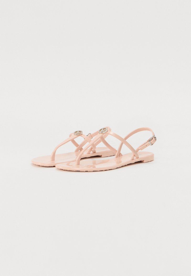 Sandales en jelly roses avec une semelle plate, dotées de brides croisées et d'accents métalliques ronds. Texture lisse avec une finition brillante.