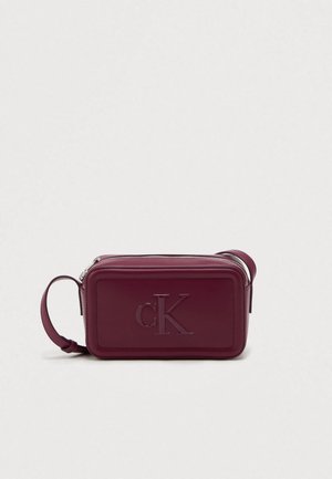 Bolso de mano de cuero burdeos con forma rectangular, logo "cK" embosado en la parte frontal, cierre mediante cremallera y una correa desmontable para llevar.