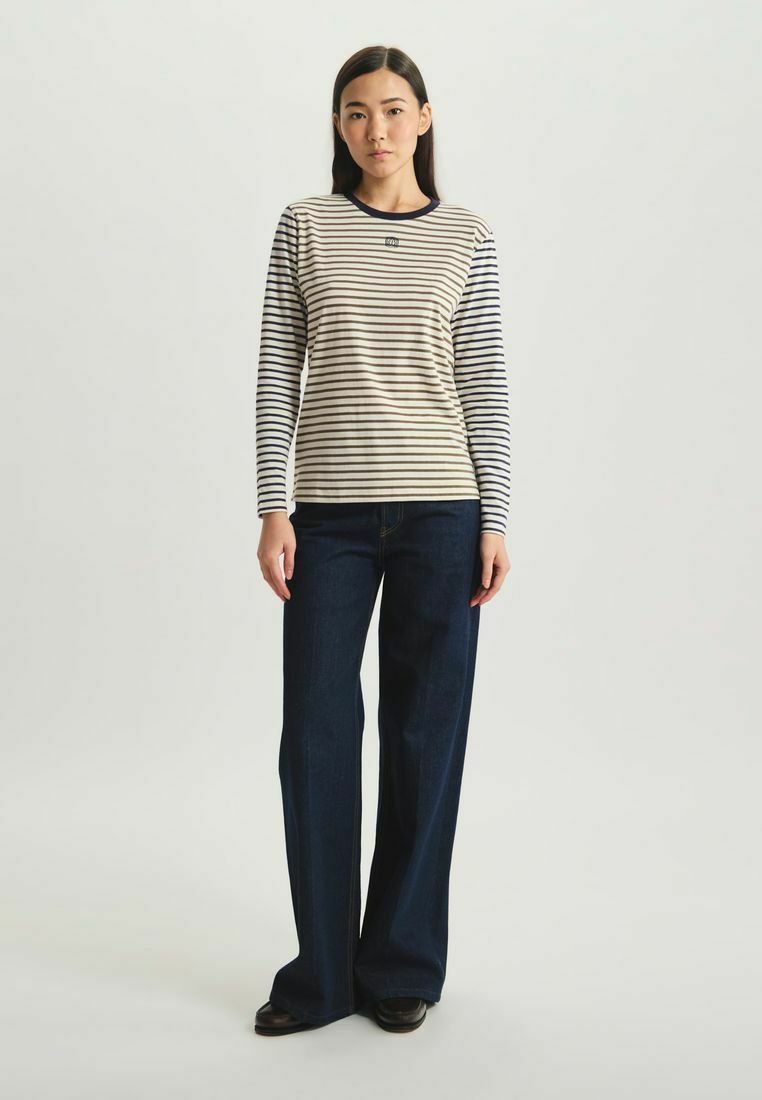 Haut à manches longues rayé en crème et marine, avec un col rond et une coupe droite. Associé à un jean évasé bleu foncé et des chaussures noires.