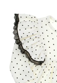 Biała sukienka z tkaniny w czarne grochy, z falbanami na rękawach wykończonymi czarną koronką. Miękka faktura i okrągły dekolt.