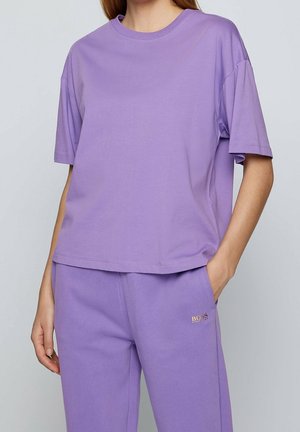 Fioletowy bawełniany t-shirt z krótkim rękawem i okrągłym dekoltem, o luźnym kroju, z detalem logo na przodzie. Spodnie w dopasowanym kolorze.