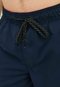 Pantaloni da bagno blu navy con una cintura elastica e un laccetto nero con dettagli bianchi. Il tessuto sembra leggero e liscio.