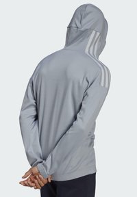 Lichtgrijze hoodie met een textuurstof, voorzien van drie witte strepen over de schouders en lange mouwen.