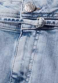 Lyseblåt denim med en sølvknap og et tyndt denimbælte, der er trukket gennem en dobbelt metalring ved taljen.