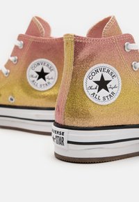 Wysokie trampki Converse z gradientowym połyskiem od różowego do złotego, z białymi sznurówkami i czarną gwiazdą na kostce.