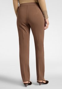 Bruine, op maat gemaakte broek met een gladde textuur en een aansluitende tailleband. Ontwerp met rechte pijpen en een subtiele vouw. Hakken zichtbaar.
