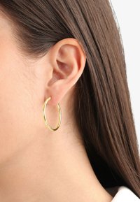 Orecchino a cerchio dorato attaccato all'orecchio, caratterizzato da un design sottile e liscio con una finitura lucida e una forma arrotondata.