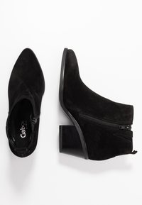 Botines de ante negro con puntera afilada, detalle de cremallera horizontal y tacón ancho. Textura suave y diseño sencillo.