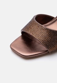 Sandale ouverte métallique marron avec une large sangle ornée de strass et un détail carré à l'avant sur fond blanc.