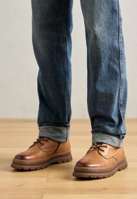 Scarpe in pelle marrone con lacci e punta arrotondata, suola in gomma e cuciture dettagliate. Indossate con jeans in denim blu con risvolti.