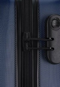 Valigia rigida con un'esterno blu testurizzato, zip nera e meccanismo di doppia chiusura. Il design include modelli distintivi per una presa migliore.