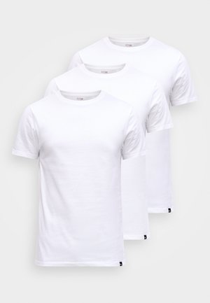 Tři jednoduchá bílá trička s krátkým rukávem a kulatým výstřihem, naskládaná mírně přes sebe na světle šedém pozadí.