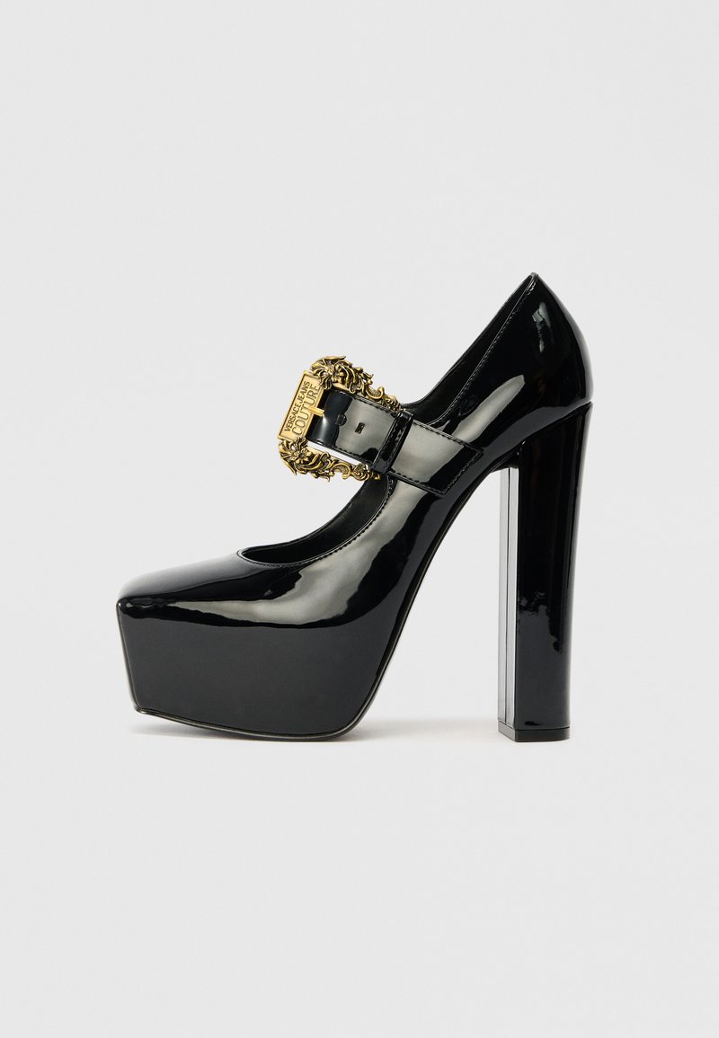 Zapatos de tacón alto de charol negro con plataforma y tacón grueso. Cuenta con una hebilla decorativa dorada y un diseño de puntera redondeada.