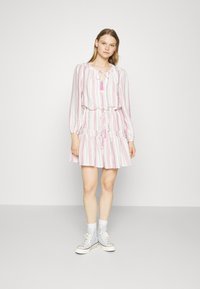Hvit kjole med rosa vertikale striper, med snøring i midjen, volangkant og lange ermer. Kombinert med lyseblå høy-top sneakers.