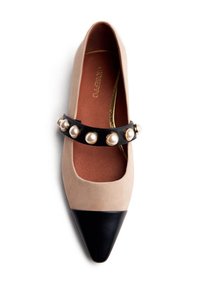 Scarpa piatta in suede beige con punta a forma di punta in pelle nera e una fascia decorativa nera con perle rotonde. Rivestimento interno dorato visibile.