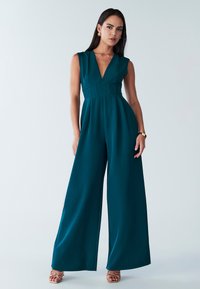 Combinaison teal avec un décolleté en V profond, taille ajustée et design à jambes larges. Fabriquée en tissu lisse, elle présente une construction sans coutures et des détails minimalistes.