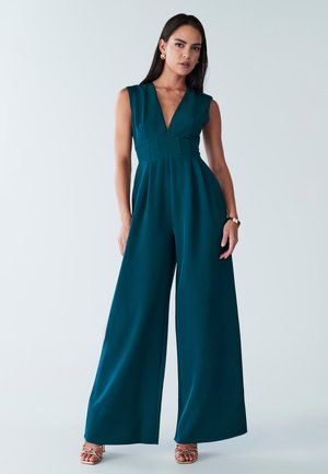 Combinaison teal avec un décolleté en V profond, taille ajustée et design à jambes larges. Fabriquée en tissu lisse, elle présente une construction sans coutures et des détails minimalistes.