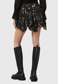 Saia preta com padrão floral, adornada com camadas de babados, combinada com botas de couro pretas até ao joelho com um design elegante e solas robustas.