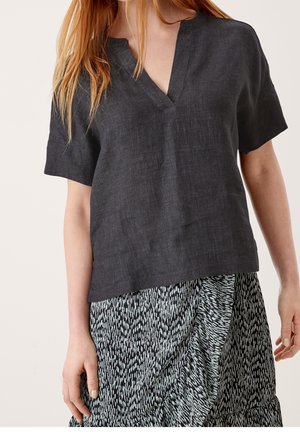 Kobieta ubrana w ciemnoszary top z krótkim rękawem i dekoltem w serek oraz czarno-białą spódnicę zapinaną na zakładkę z wzorem.