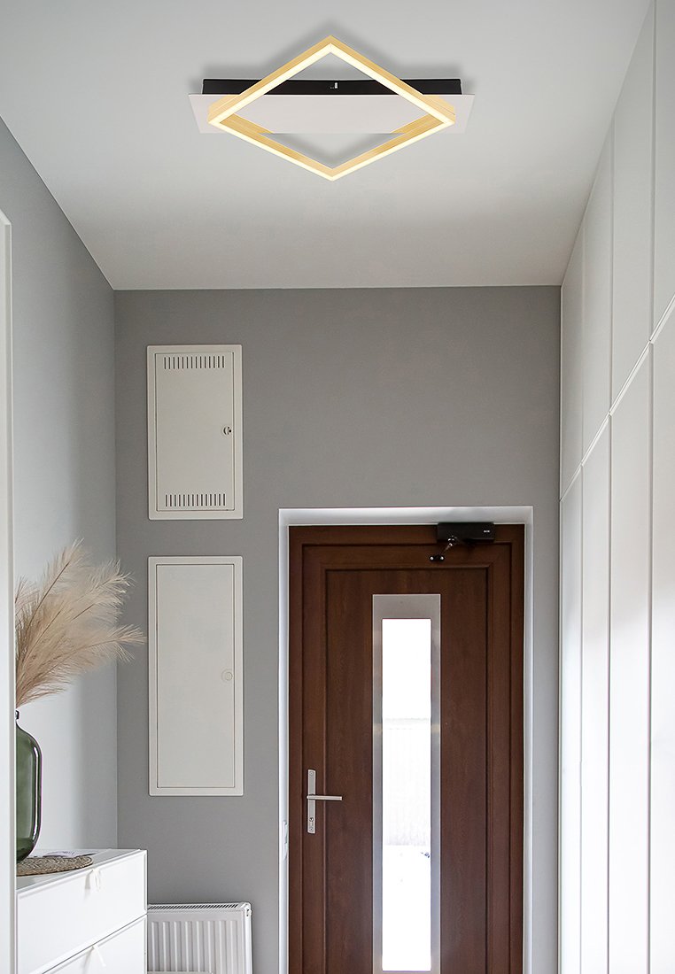 Luz de techo cuadrada con un marco negro y un suave brillo amarillo. Colocada en un pasillo moderno con paredes grises y una puerta de madera.