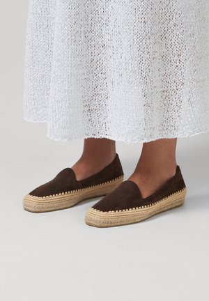 Espadrillas senza lacci in suede marrone scuro con suola platform intrecciata in juta, indossate con una gonna bianca di maglia che lascia scoperti polpacci e caviglie.