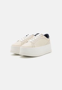 Sneakers na platformie w beżowej skórze z teksturowaną białą podeszwą. Posiadają białe sznurówki i ciemnoniebieski tył. Złote akcenty w postaci oczek.