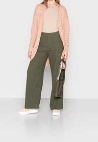 Ljust rosa stickad cardigan, beige topp, olivgröna vida byxor och krämfärgade platåskor, med en grön axelväska.