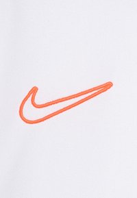 Pomarańczowy haftowany logo swooshu Nike na białym teksturowanym tle.