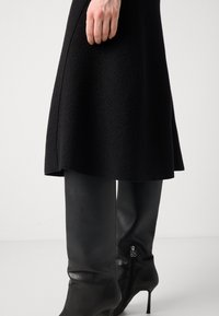 Black flared skirt in a textured fabric, paired with knee-high black leather boots featuring a zipper detail and slim high heels.