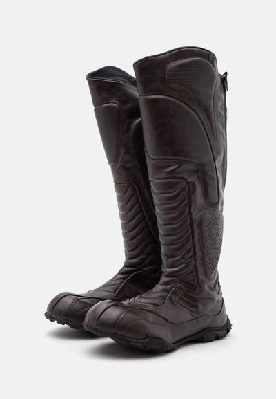 Bottes de moto hautes en cuir marron foncé avec zones rembourrées et renforcées et semelles en caoutchouc texturées.