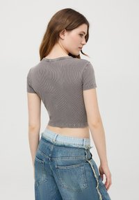 Crop top grigio a coste con maniche corte, con un colletto rotondo. Abbinato a jeans in denim a vita alta strappati.
