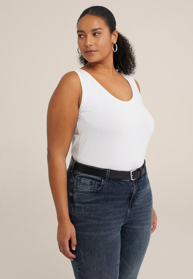 Top blanco sin mangas combinado con jeans azul oscuro y un cinturón negro. El top tiene un escote redondeado, mientras que los jeans presentan una textura de denim desgastado.