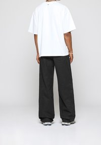 T-shirt blanc oversize à manches courtes, associé à un pantalon noir à jambes larges avec broderies florales et baskets à semelles en caoutchouc.