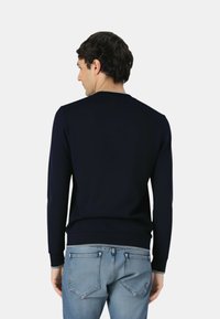 Dunkelblauer Pullover mit Rundhalsausschnitt, gerippten Bündchen und Saum. Glatte Textur, taillierte Passform, getragen mit hellblauen Jeans.