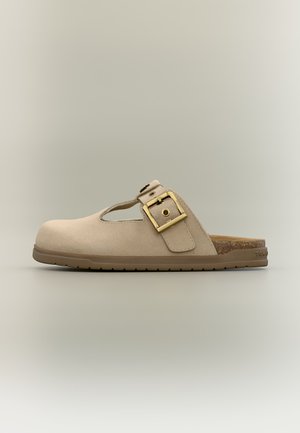 Sandale beige en daim à enfiler avec des côtés ouverts, une large bride à boucle dorée et une semelle marron rainurée.