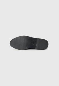 Black shoe sole featuring a textured grip pattern and a rounded shape, with a circular logo embossed near the center.