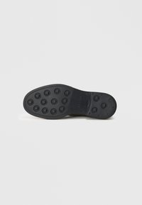 Suela de zapato de goma negra con dibujos circulares, diseño plano y marca sutil. Textura suave y bordes redondeados para un uso cómodo.