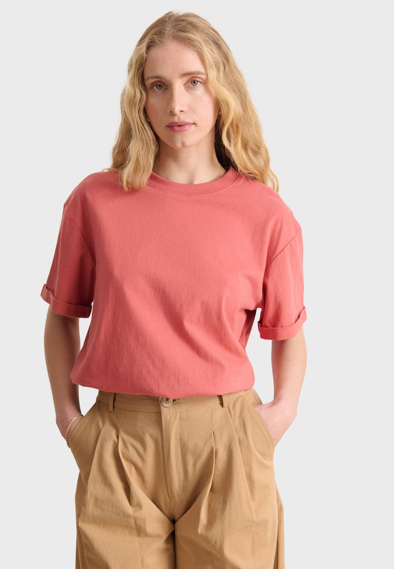 Damask pink bomull t-shirt med uppvikta ärmar, som är matchad med beige veckade byxor. Tyget ser mjukt och strukturerat ut.