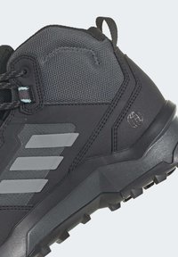 Botte de randonnée noire et grise avec tige en mesh, languette, trois bandes grises sur le côté et semelle robuste à crampons.