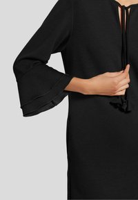 Schwarzes Kleid mit V-Ausschnitt und Bindeschluss. Verfügt über glockenförmige Ärmel mit einer glatten Textur und einem subtilen Glanz am Saum.