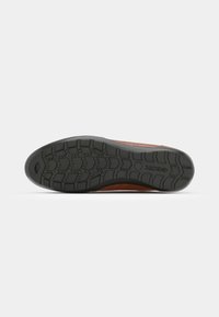 Sneaker with a brown leather upper and a black rubber sole. Features a textured surface with a tread pattern for grip and support.