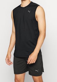 Canotta atletica nera senza maniche con colletto rotondo e logo grigio sul petto, abbinata a pantaloni corti sportivi neri con accenti del logo.