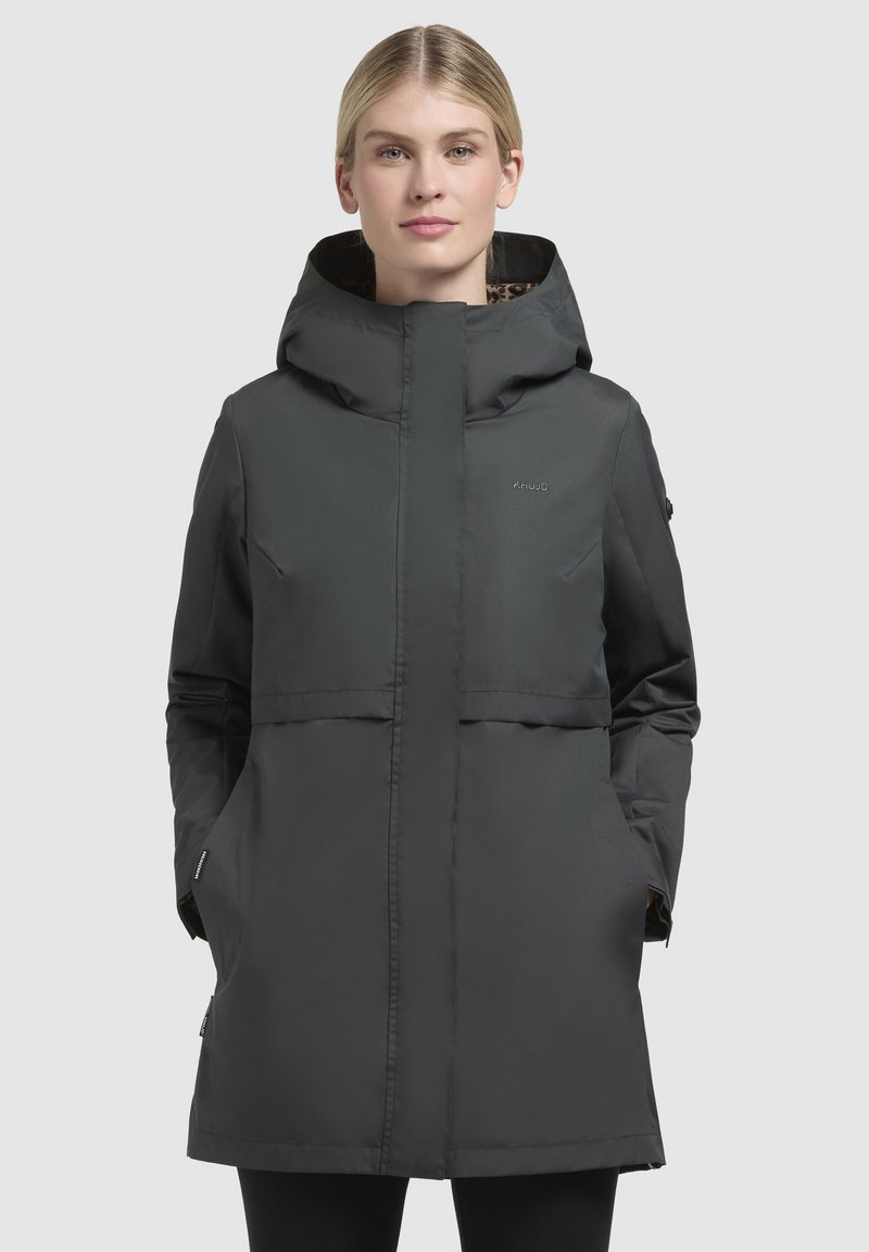 Zwarte caputch jacket met een ritssluiting, voorzien van twee zijzakken, een middellange snit en een subtiele logo op de borst. Textuur voering zichtbaar in de capuchon.