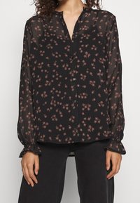 Sort gennemsigtig bluse med små pink blomstermønstre, lange ærmer med sammensnørende mansjetter og knaplukkning foran. Let og flowy tekstur.
