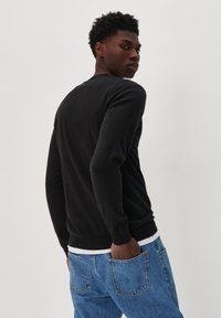 Black long-sleeve sweater made of smooth fabric with a round neck and ribbed cuffs, paired with blue denim jeans. Minimal detailing.
