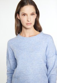 Lichtblauwe trui met een textuur en een zachte afwerking. Heeft een ronde halslijn en een relaxte fit met verlaagde schouders.