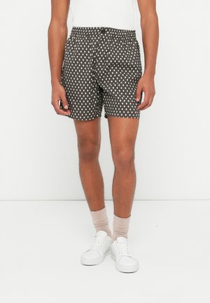 Shorts pour hommes à motifs avec un fond noir et des formes géométriques blanches, taille élastique et coupe décontractée. Associés à des baskets blanches.