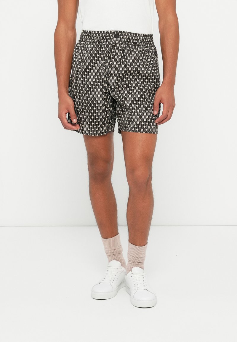 Shorts da uomo con motivo, caratterizzati da uno sfondo nero con forme geometriche bianche, vita elastica e una vestibilità comoda. Abbinati a sneakers bianche.