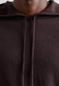 Mörkbrun hoodie i ett mjukt, strukturerat tyg. Den har en huva och en central söm, vilket visar en minimalistisk design.